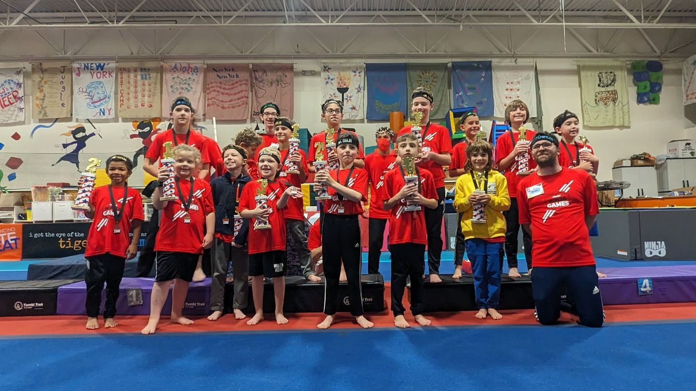 A group of children are posing for a picture in a gym holding trophies.