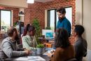 Group of colleagues in office, man presenting data on tablet, brick wall backdrop.