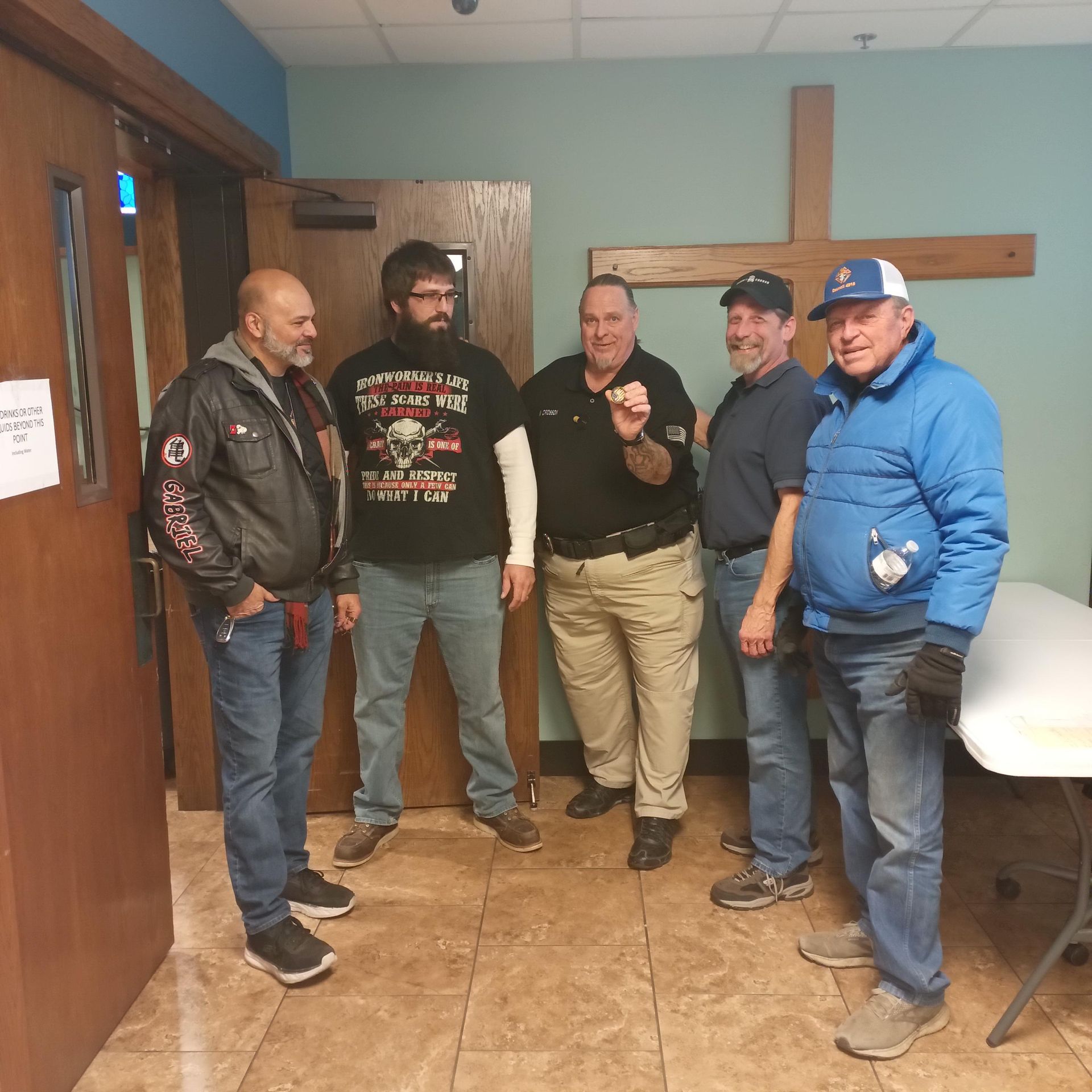 A group of men are standing in a room with a cross on the wall