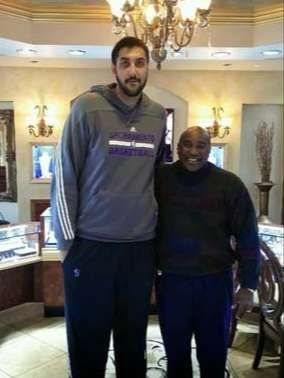 Two men are standing next to each other in a room with a chandelier.