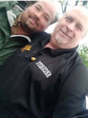 Two men are posing for a picture together . one of the men is wearing a shirt that says sheriff.