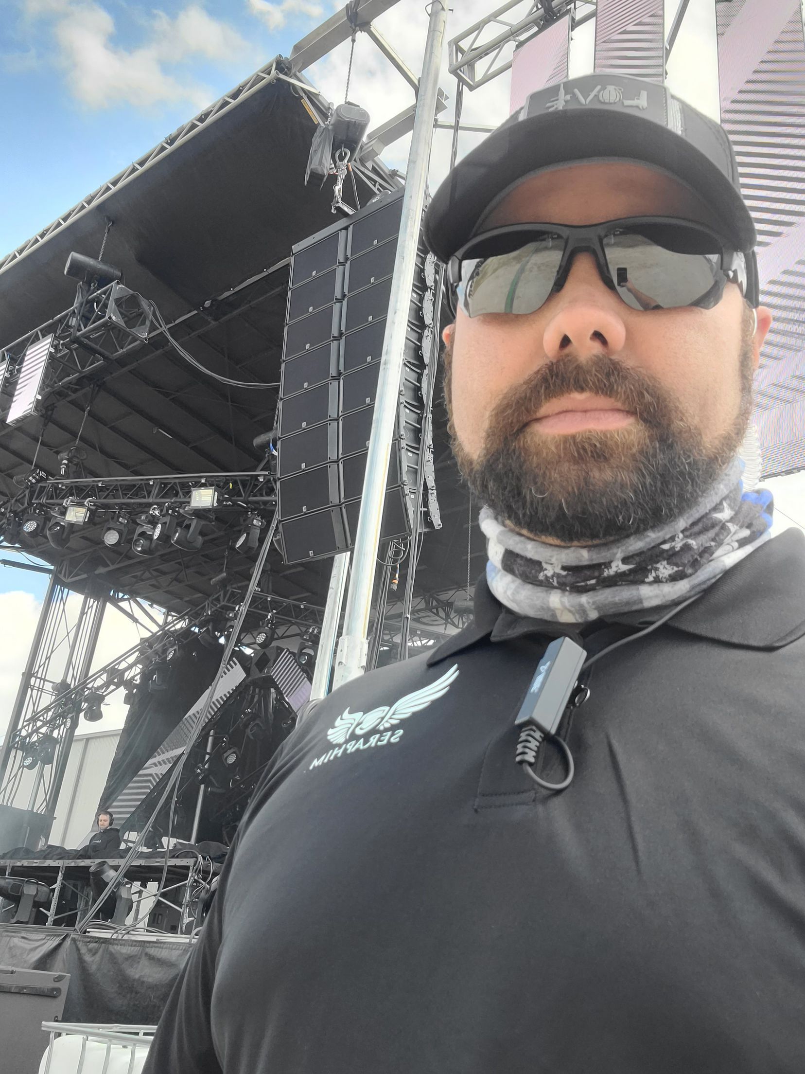 A man wearing sunglasses and a hat is standing in front of a stage.