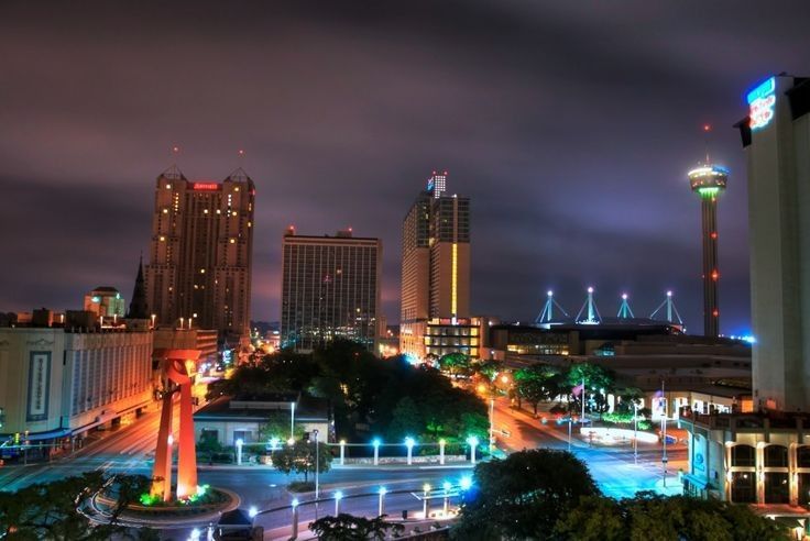 An aerial view of a city at night with a fountain in the middle.