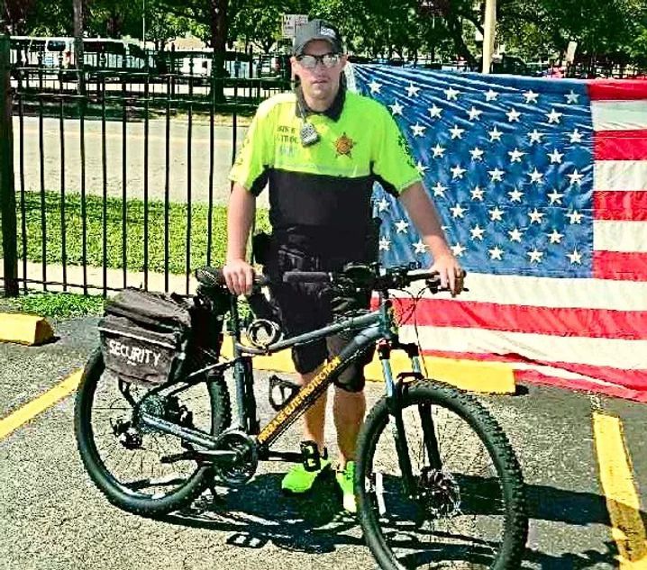 A man is standing next to a bicycle in front of an american flag.