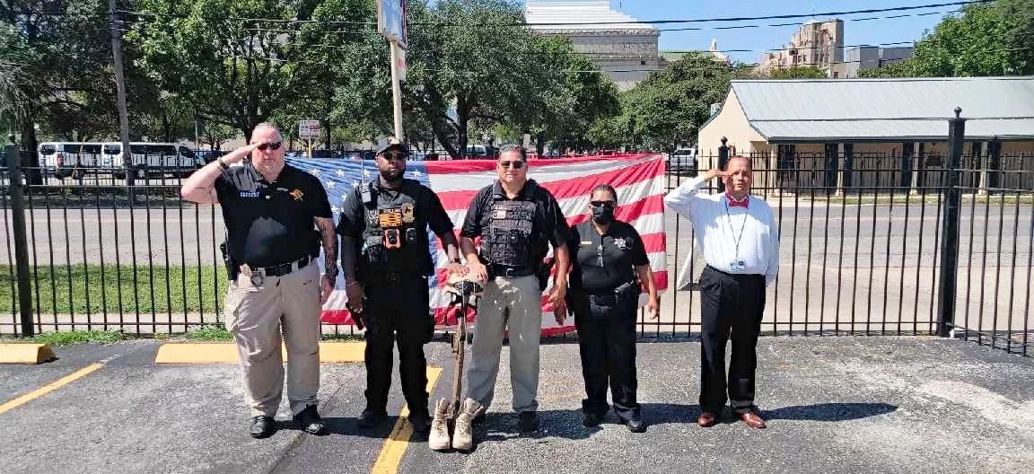 A group of men are standing in front of an american flag in a parking lot.