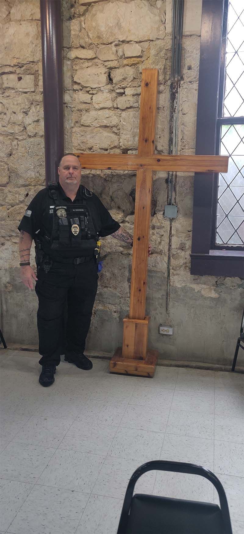 A police officer is standing next to a wooden cross in a room.