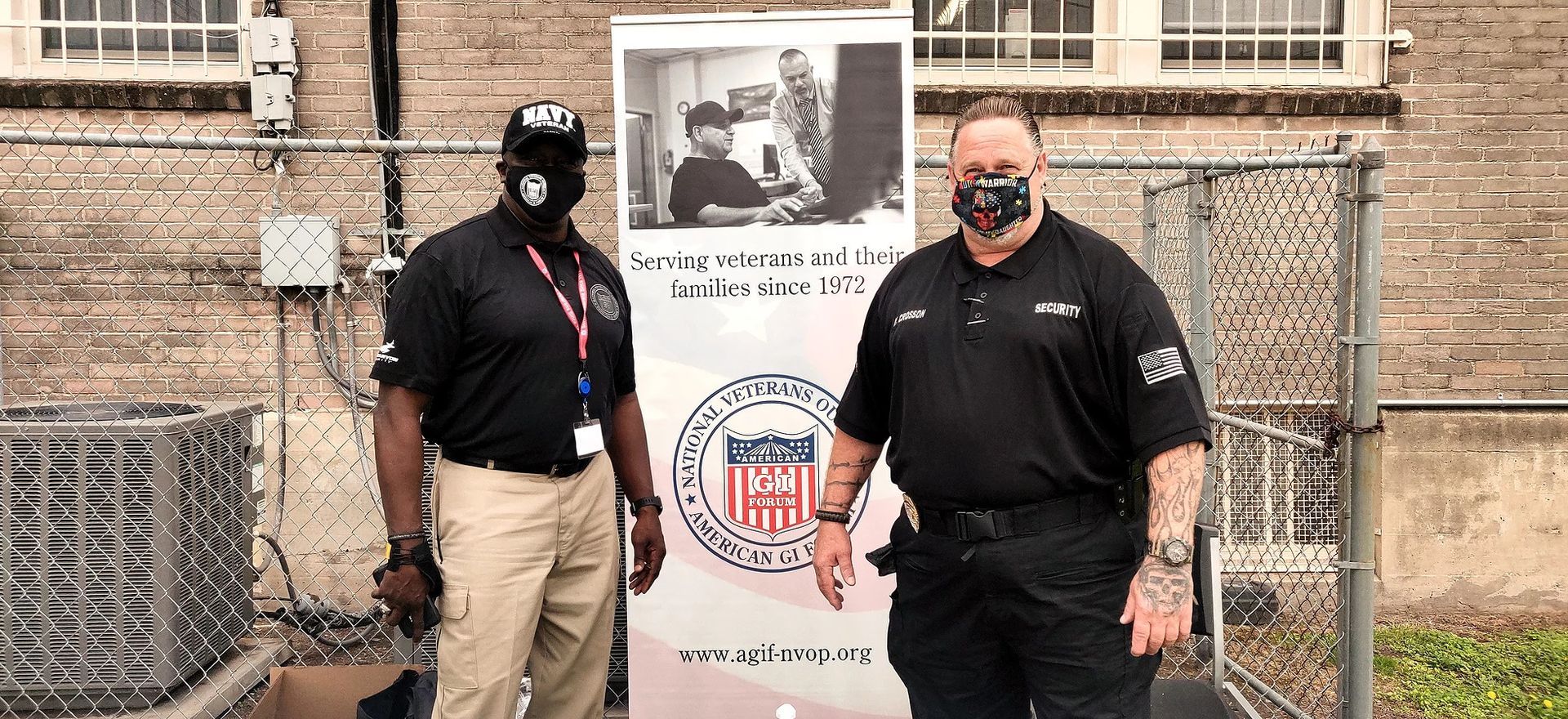 Two men wearing masks are standing next to each other in front of a sign.