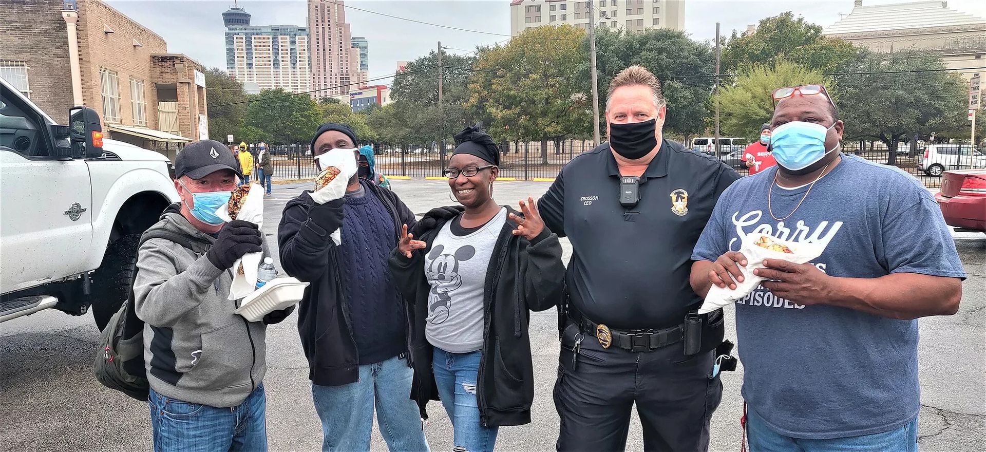 A group of people wearing face masks are standing next to each other in a parking lot.