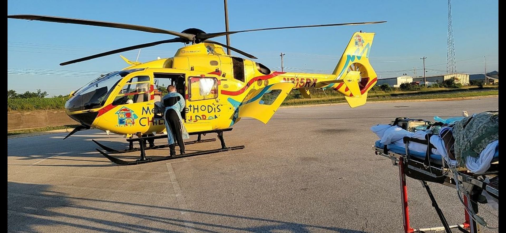 A yellow helicopter is parked on the ground next to an ambulance.