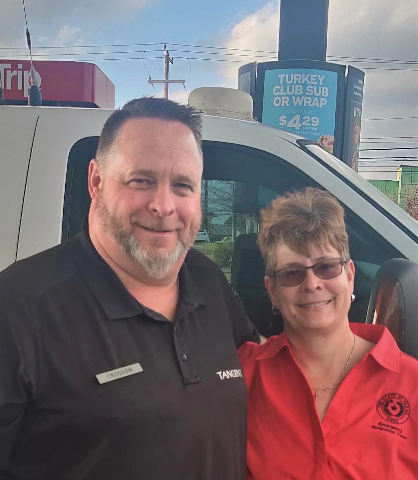A man and a woman are posing for a picture in front of a white van.