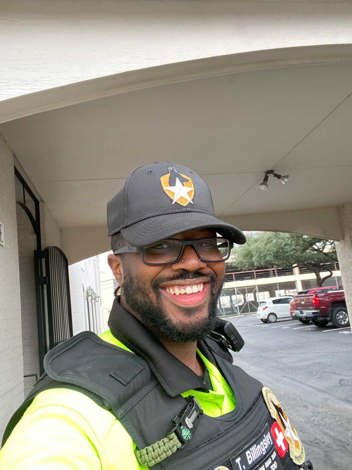A man wearing a hat , vest and sunglasses is smiling.