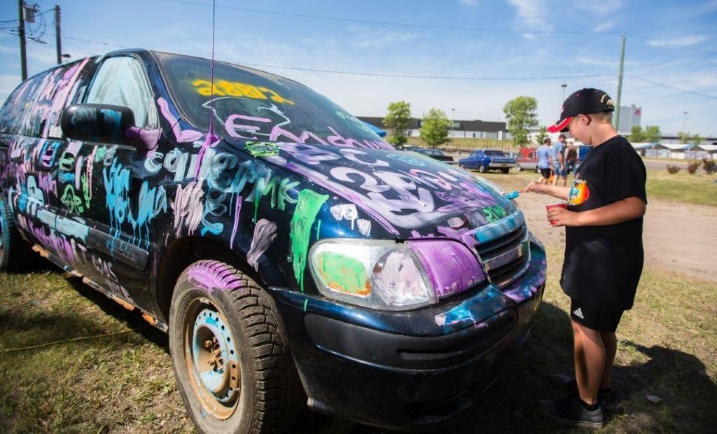 A man is standing next to a car that has been covered in graffiti.