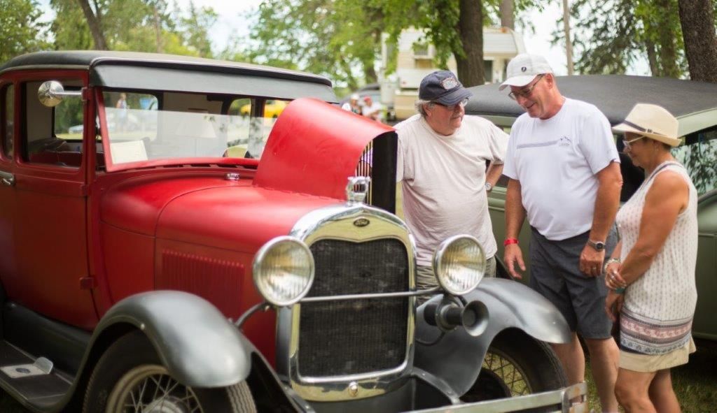 A man and a woman are looking at an old red car.