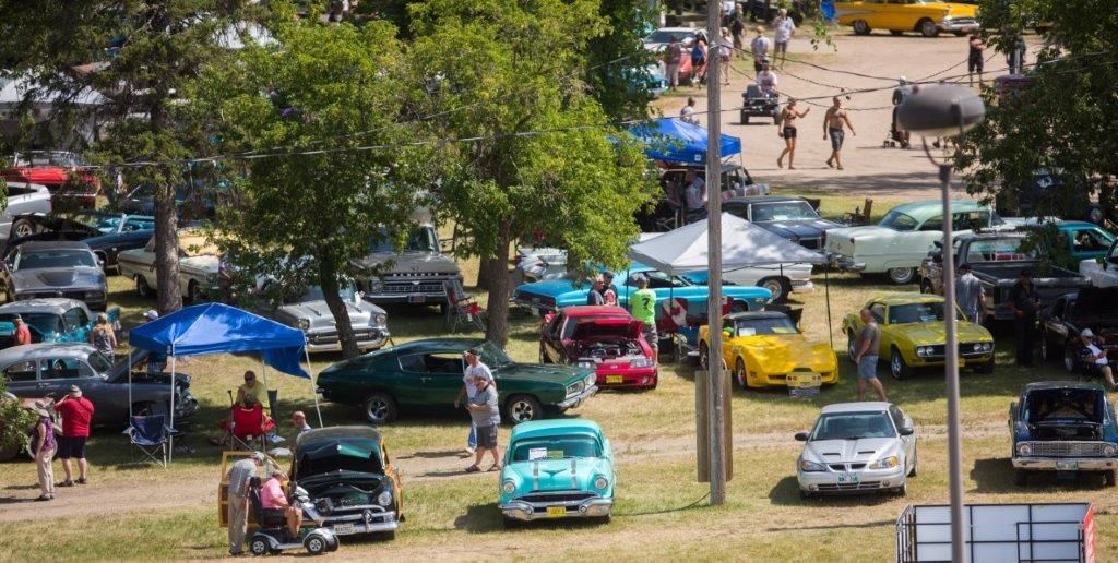 A lot of cars are parked in a field at a car show.