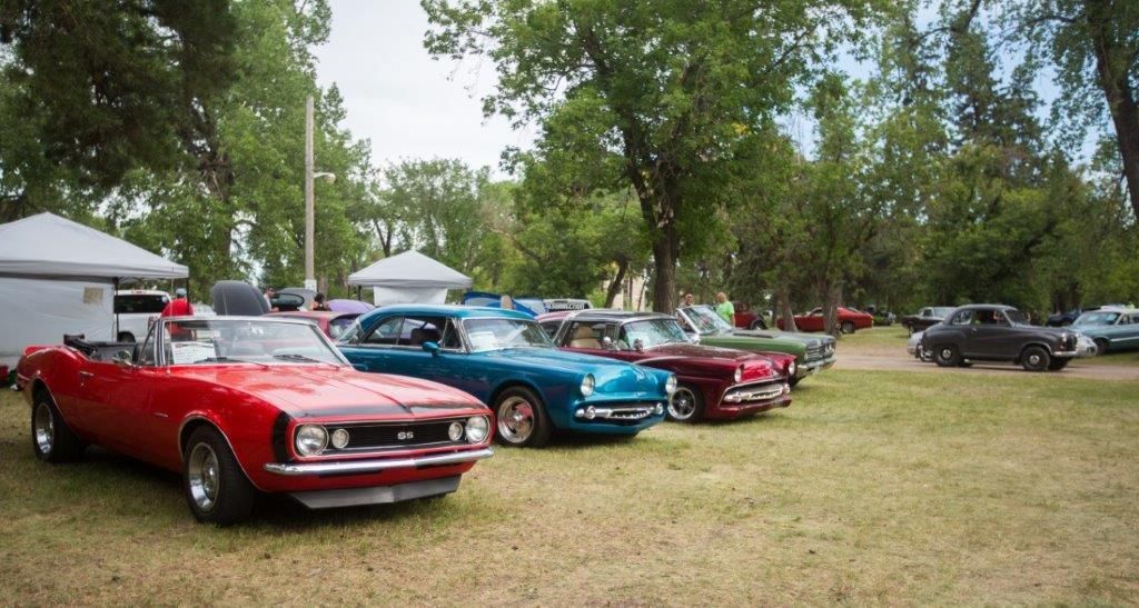 A row of cars are parked in a grassy field at a car show.