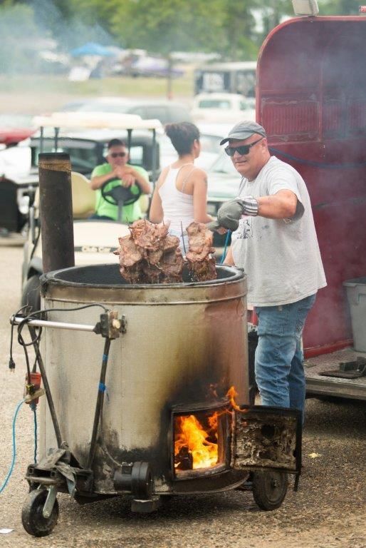 A man is cooking meat in a large pot on a trailer.