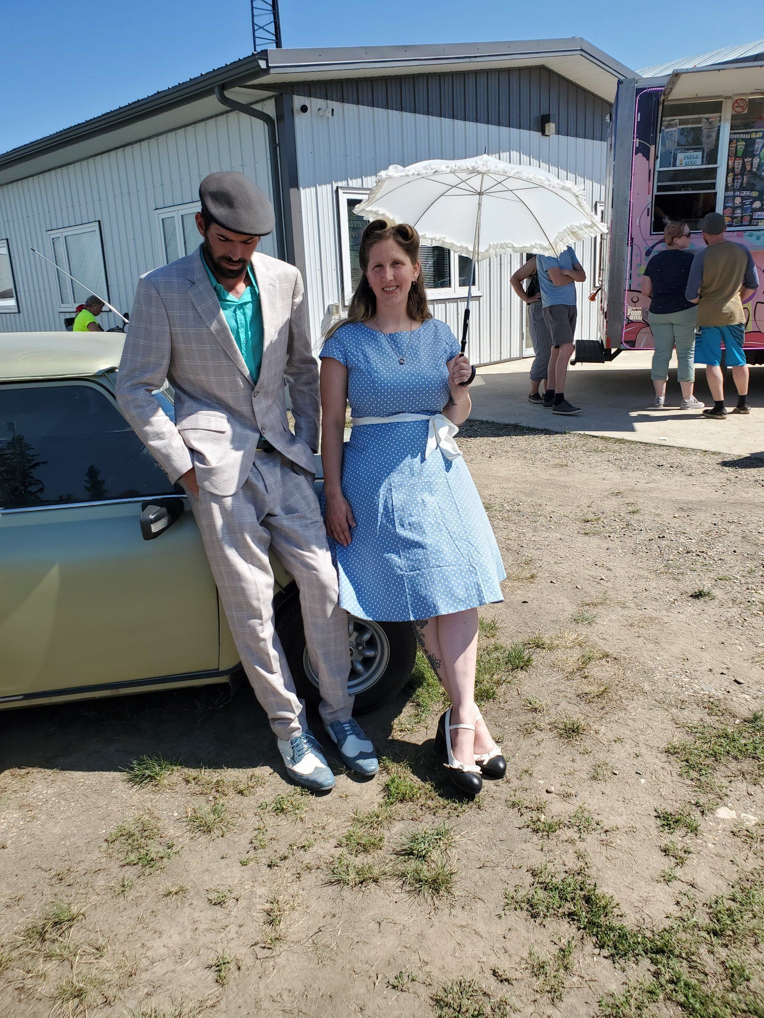 A man in a suit and a woman in a blue dress are standing next to a car.
