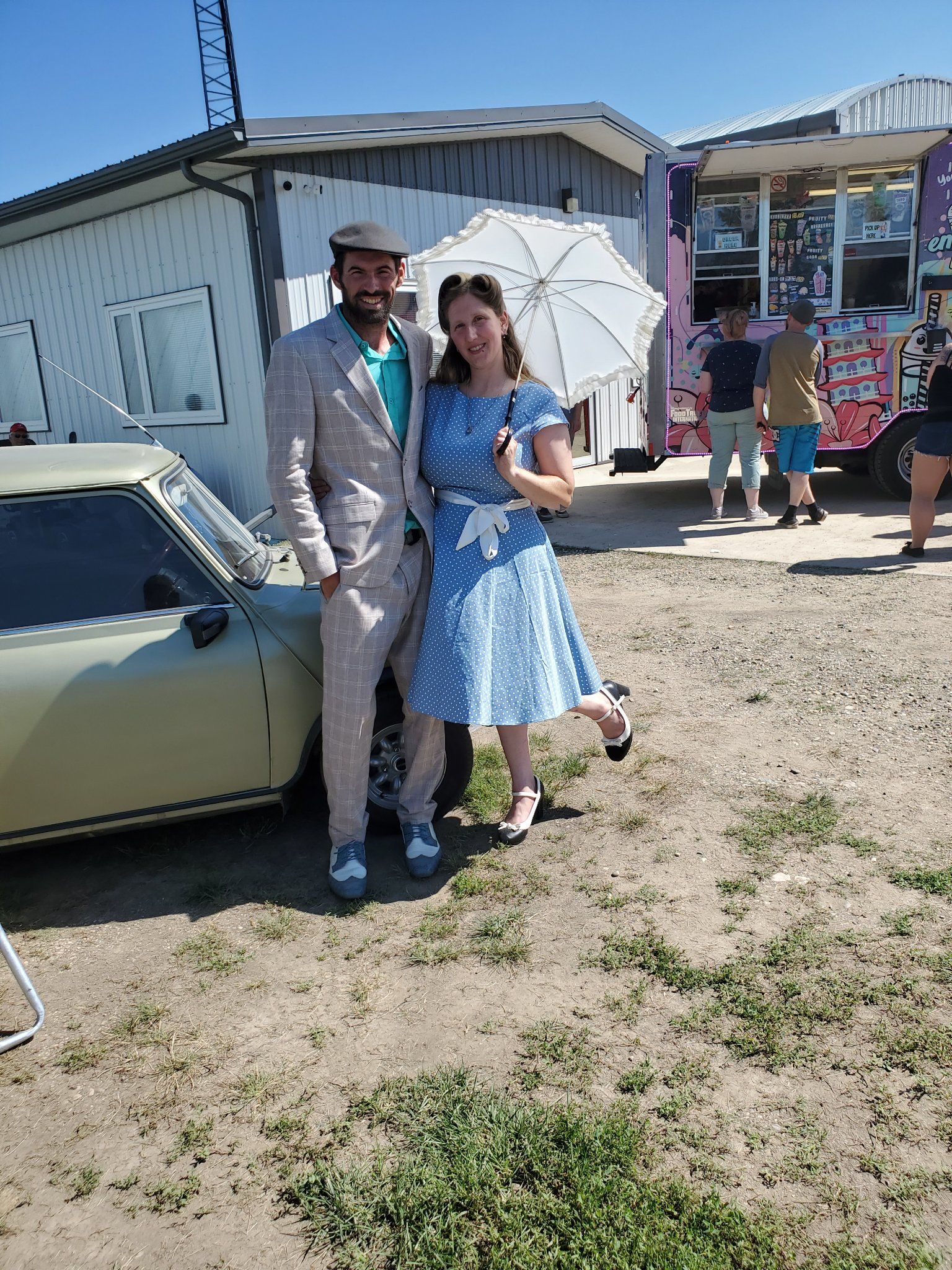 A man in a suit and a woman in a blue dress are standing next to a car.