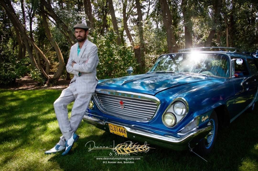 A man in a suit is leaning against a blue car.