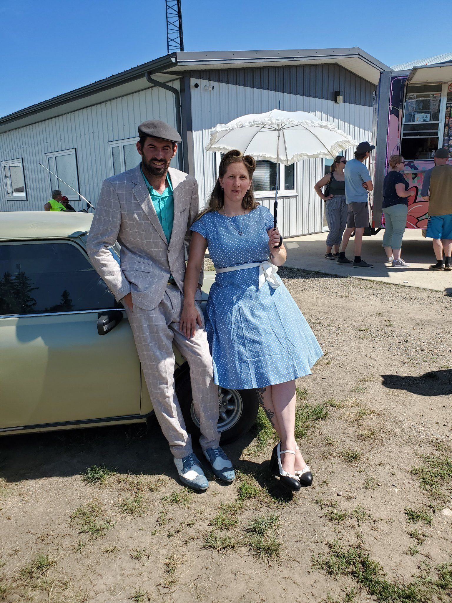A man and a woman are standing next to a car in a field.