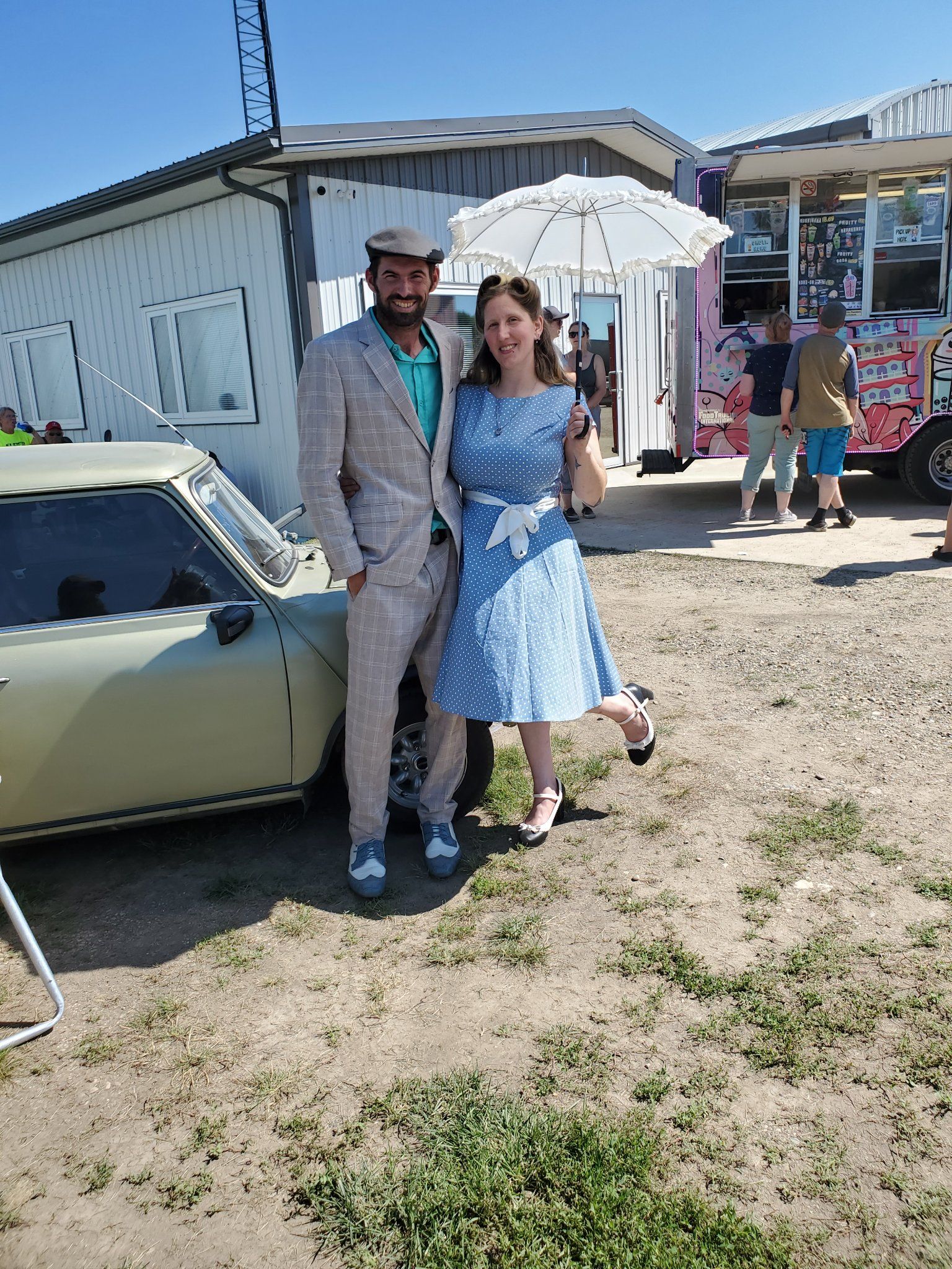 A man and a woman are posing for a picture in front of a car.