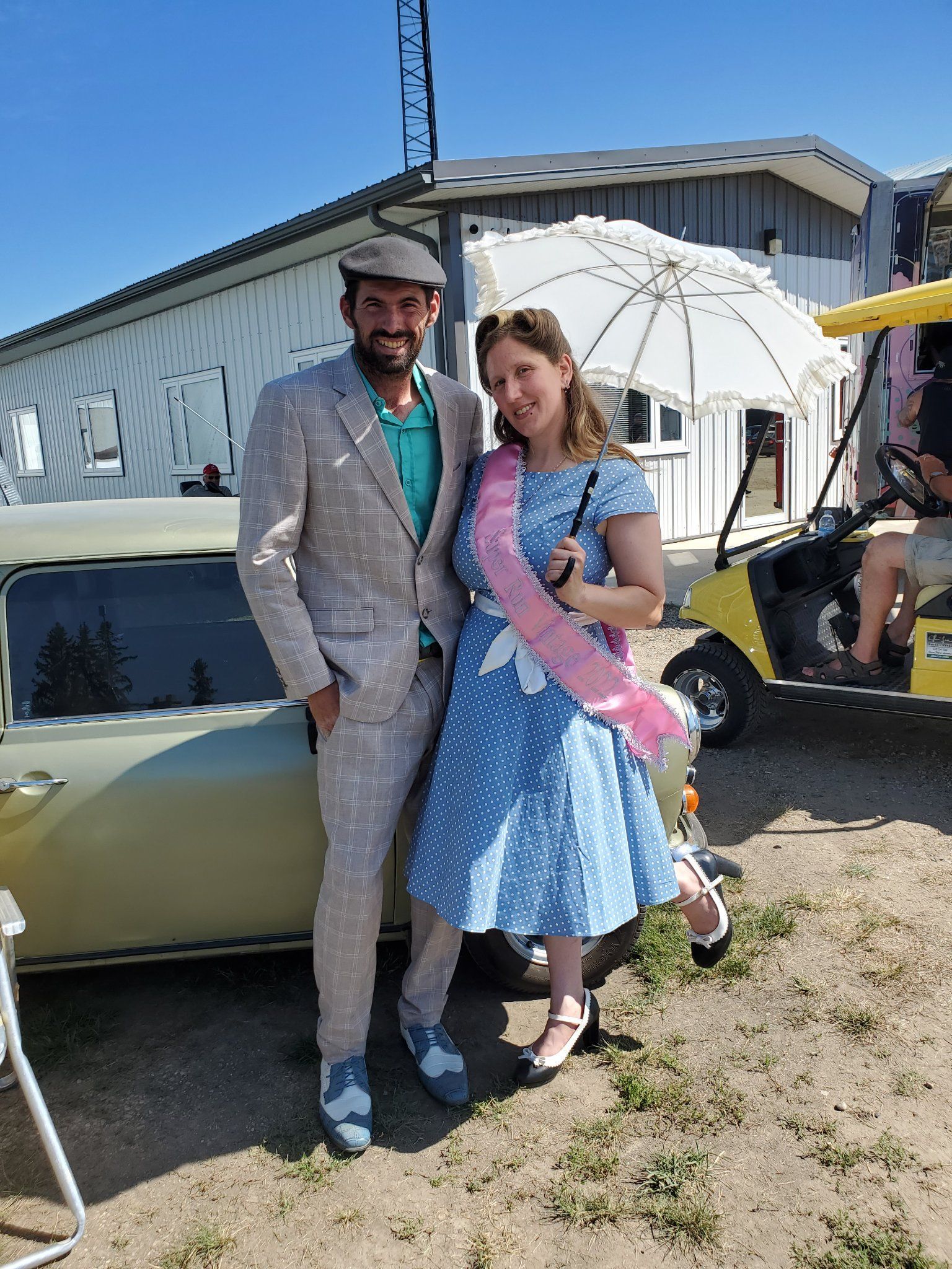A man and a woman are posing for a picture in front of a car.