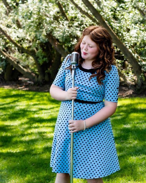 A girl in a blue polka dot dress is singing into a microphone.
