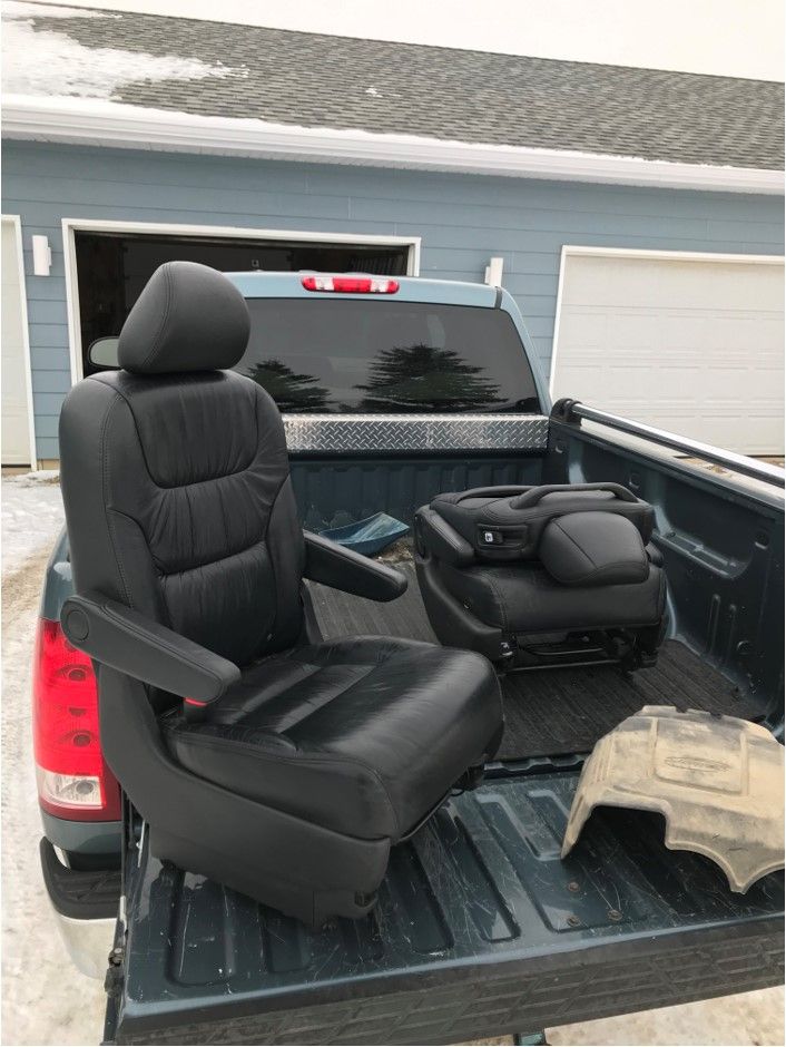 A truck with two seats in the back is parked in front of a garage.