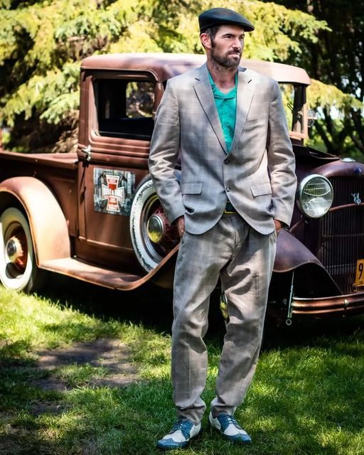 A man in a suit is standing in front of an old truck