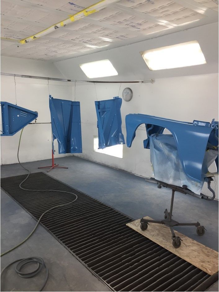 A blue car is being painted in a paint booth