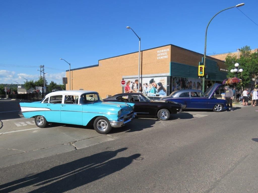 Three old cars are parked on the side of the road in front of a building.