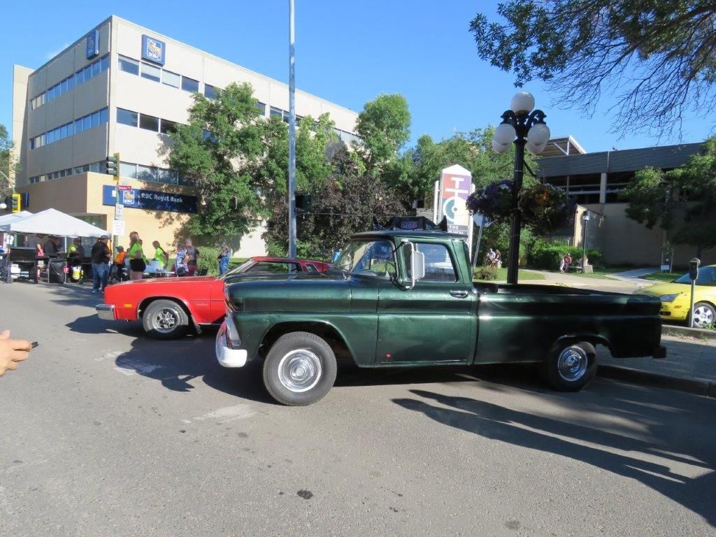 A green truck is parked on the side of the road next to a red car.