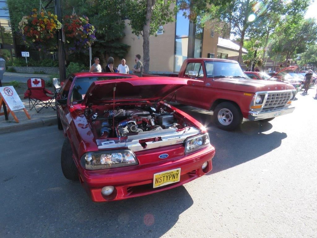 A red car with the hood up is parked next to a red truck.
