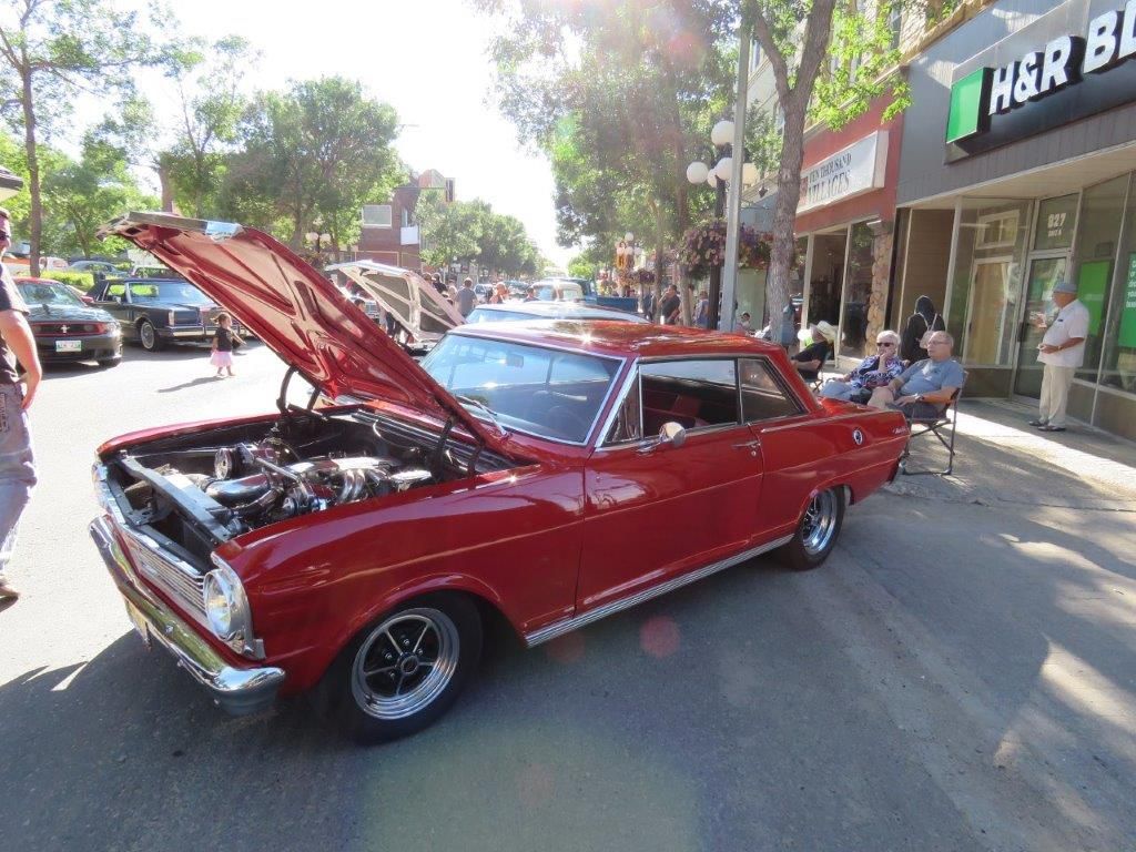 A red car with the hood up is parked on the side of the road.