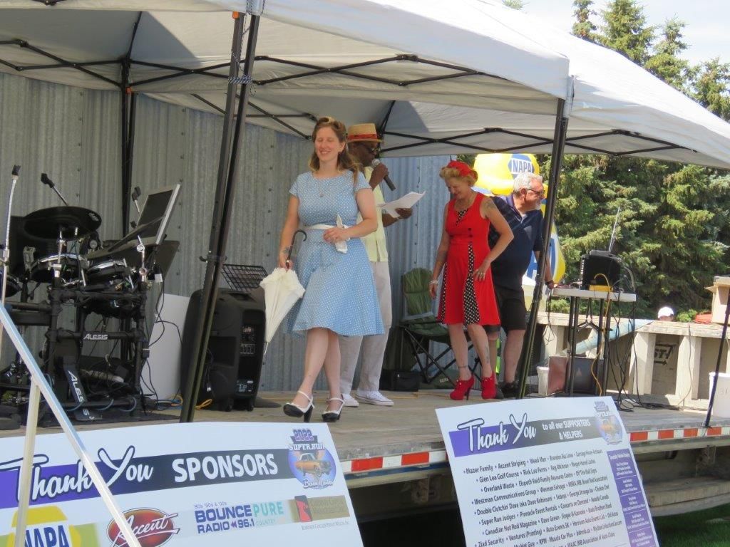 A group of women are standing on a stage under a tent holding umbrellas.