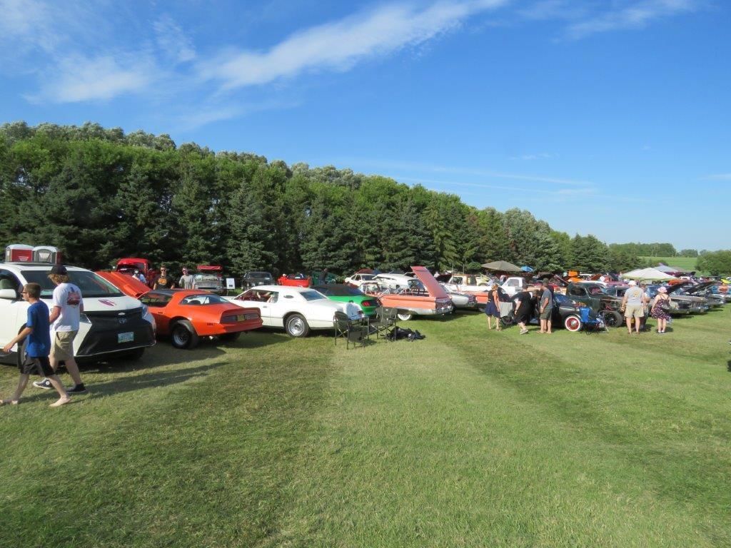 A row of cars are parked in a grassy field.