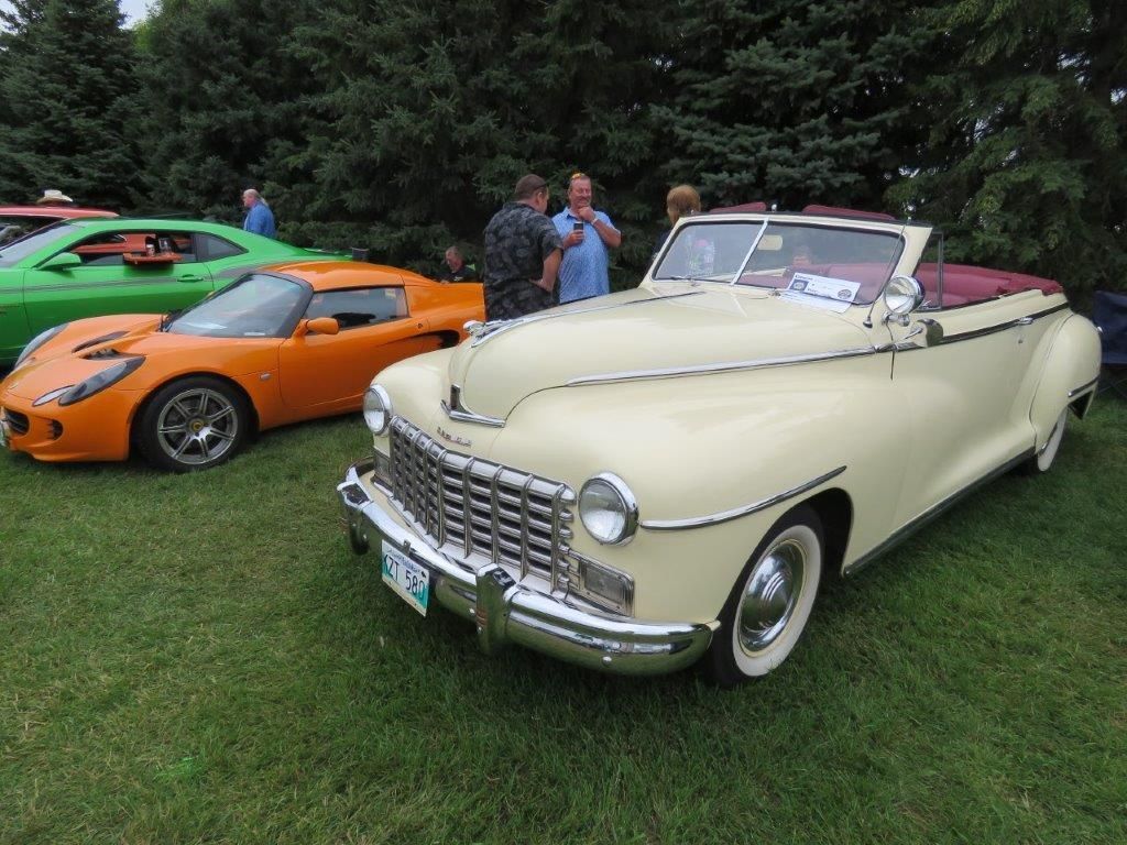 A group of people are standing around a convertible car at a car show.