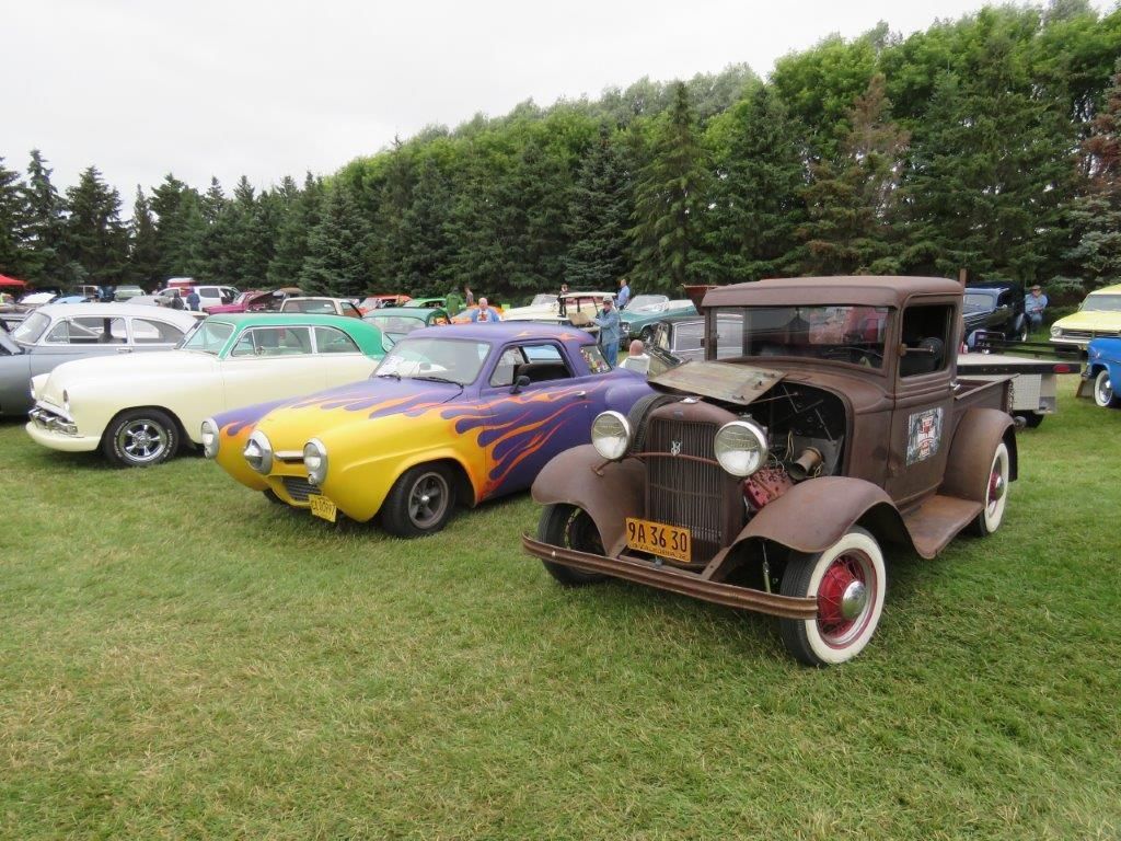 A row of old cars are parked in a grassy field.