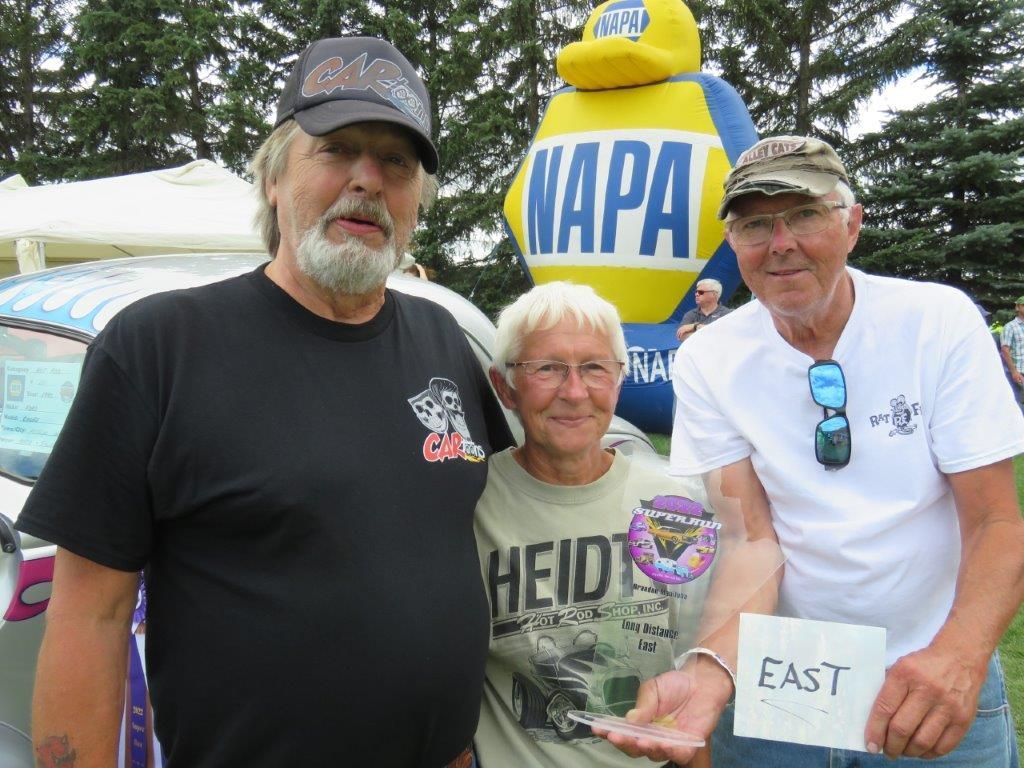 Three people are posing for a picture in front of a napa sign.