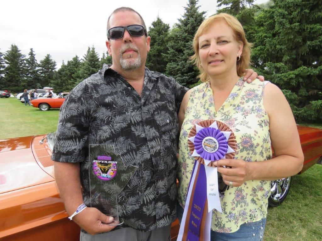 A man and a woman are posing for a picture in front of a car.