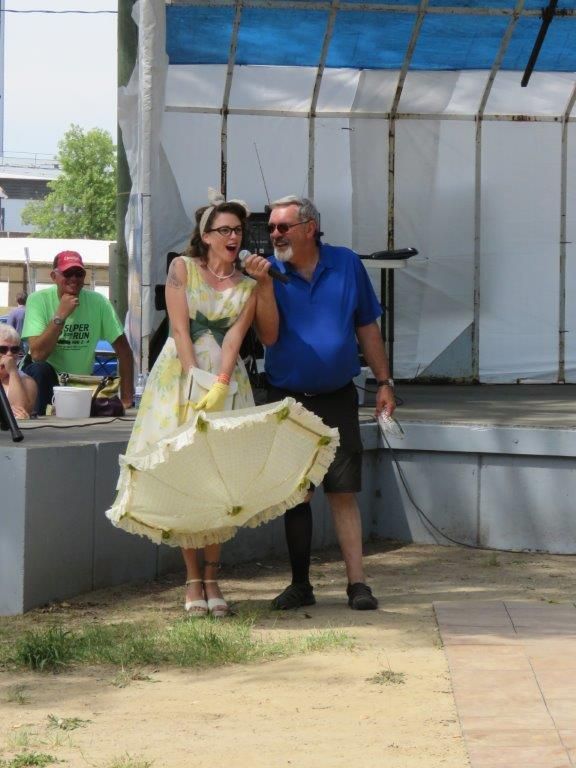 A woman in a yellow dress is singing into a microphone while standing next to a man in a blue shirt.