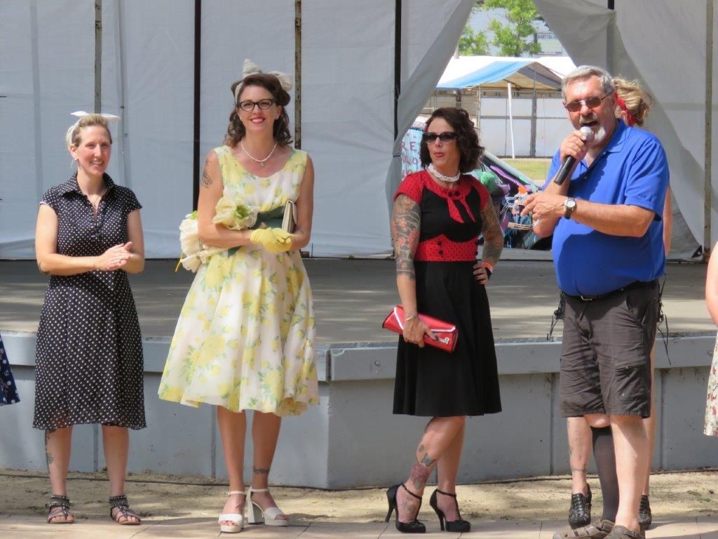 A man is speaking into a microphone while three women stand behind him