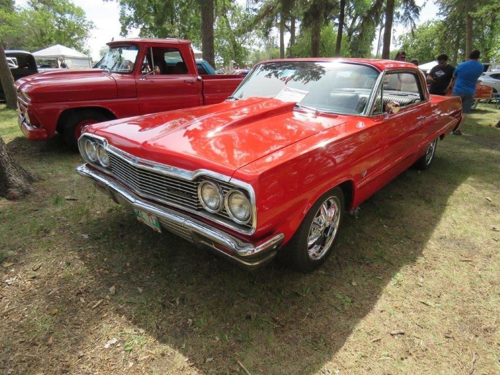 A red car is parked next to a red truck at a car show.