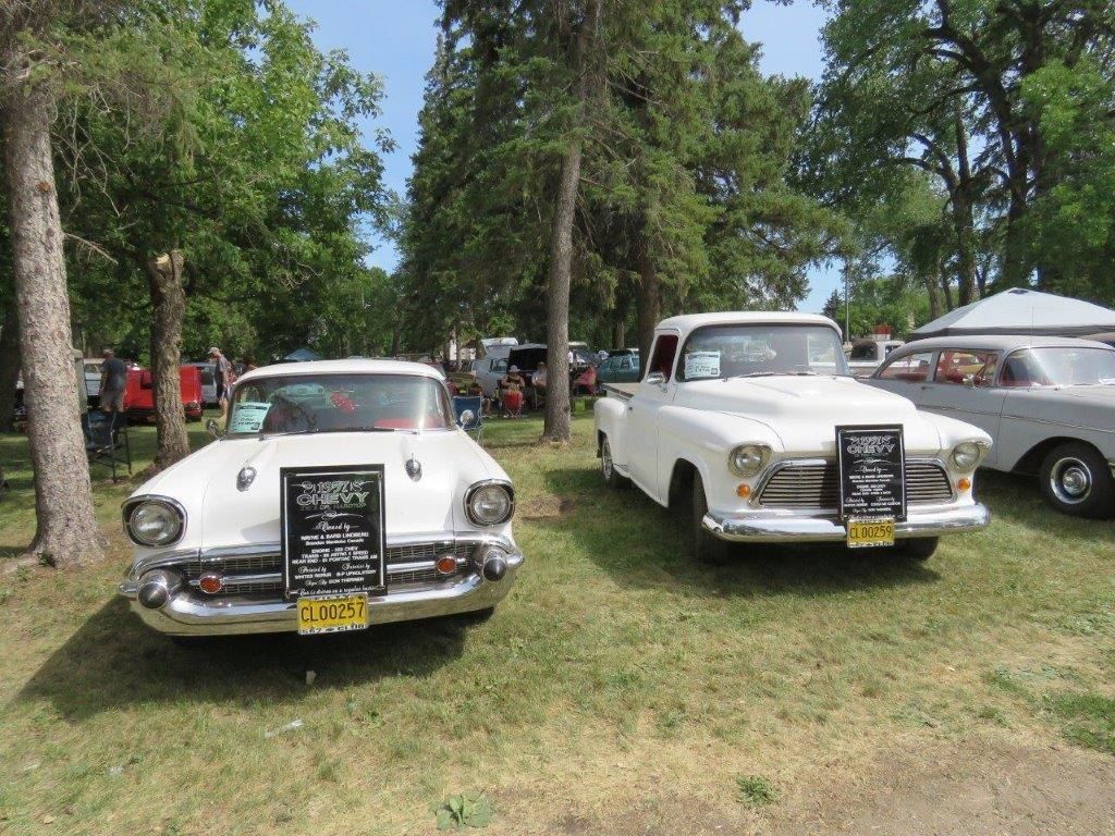 Two old cars are parked next to each other in a grassy field.
