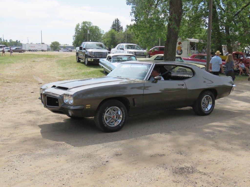 A gray car is parked in a dirt lot next to a tree.