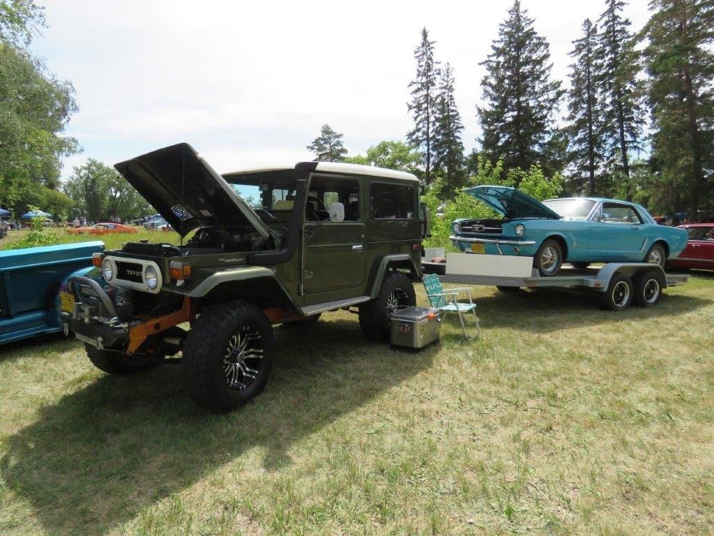 A green jeep is parked next to a blue car on a trailer.