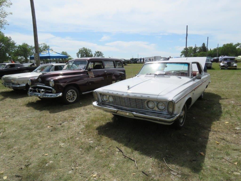 A row of old cars are parked in a grassy field