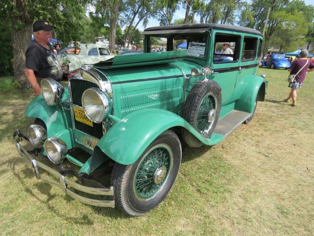 An old green car is parked in a grassy field.