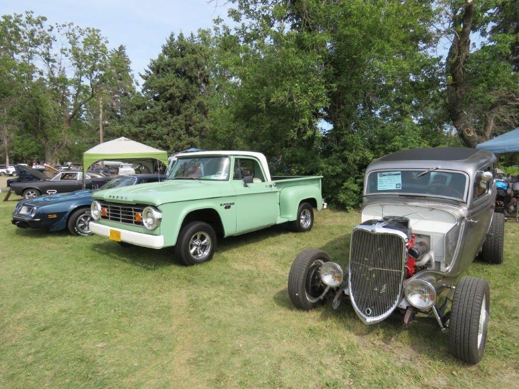 A green truck and a hot rod are parked next to each other in a grassy field.