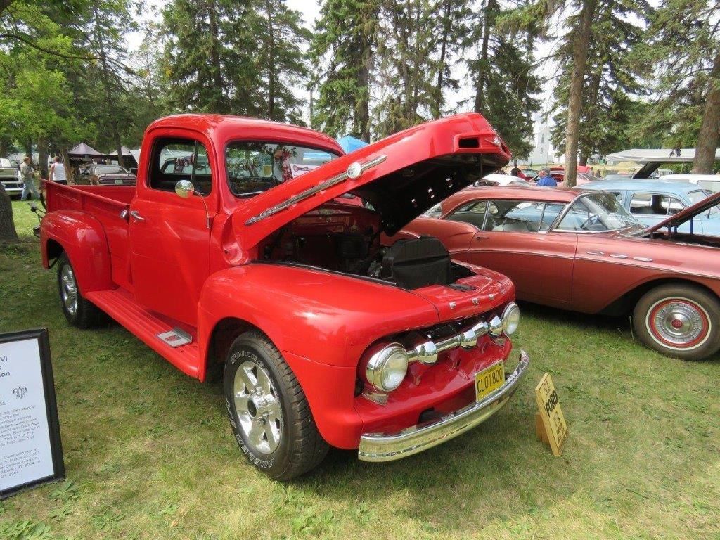 A red truck with the hood up is parked next to a pink car.